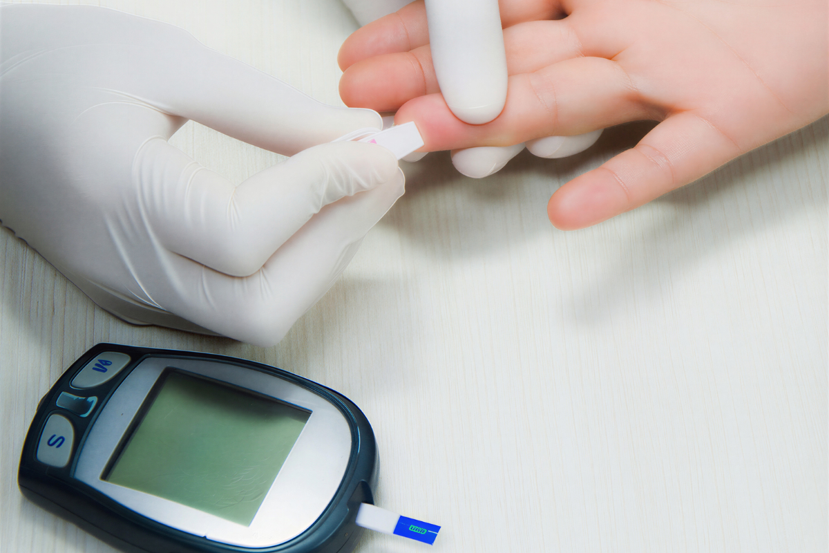 Person in medical gloves performing a finger-prick blood test next to a glucose meter