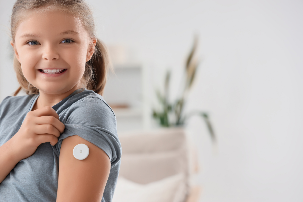 Smiling girl showing a circular glucose monitor sensor on her upper arm
