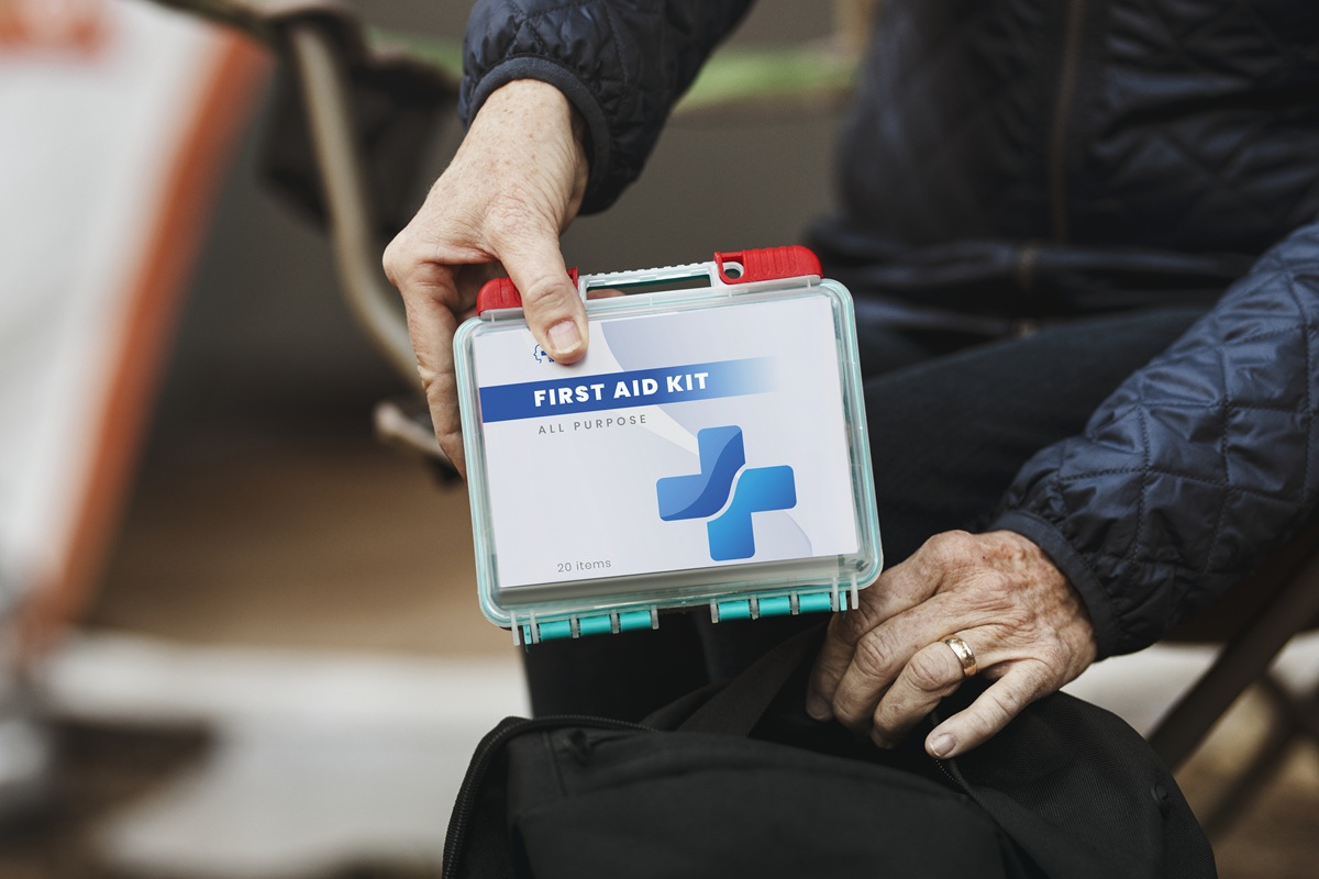Older person holding a sealed all-purpose first aid kit with both hands while seated outdoors.