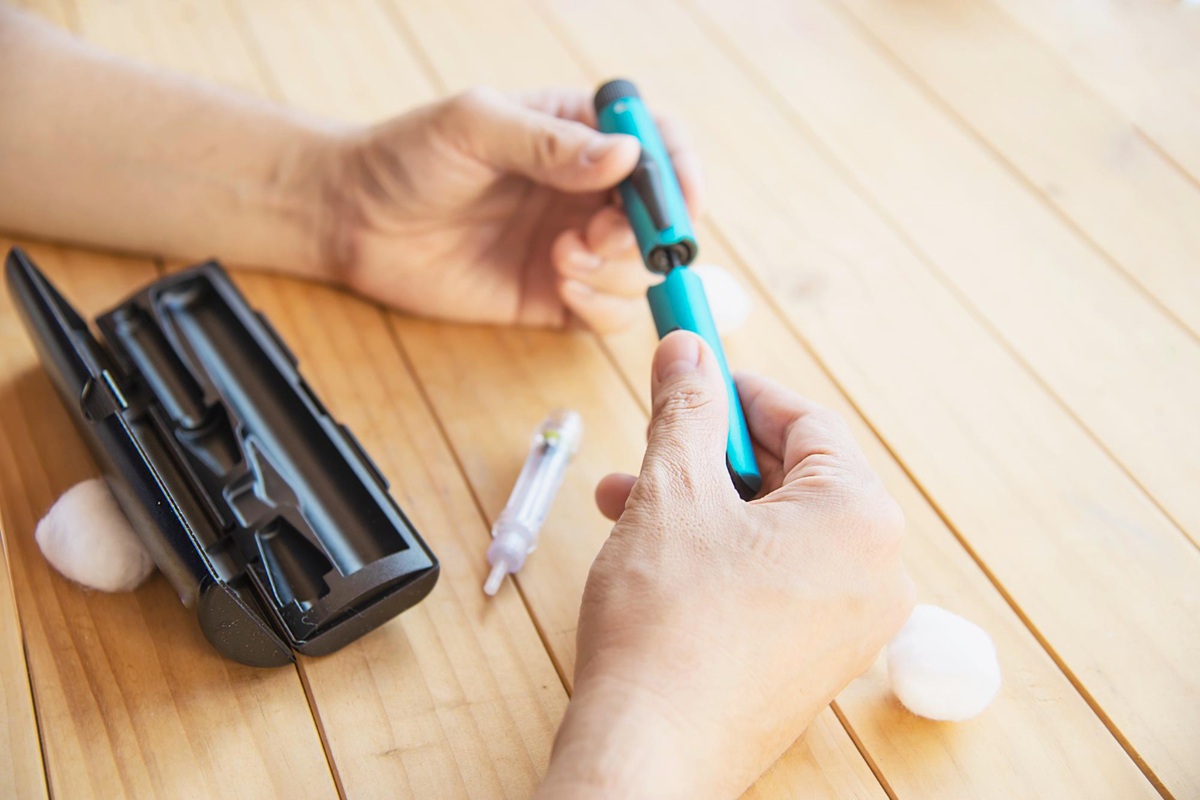Person assembling a medication auto-injector pen at a table, with related medical supplies nearby.