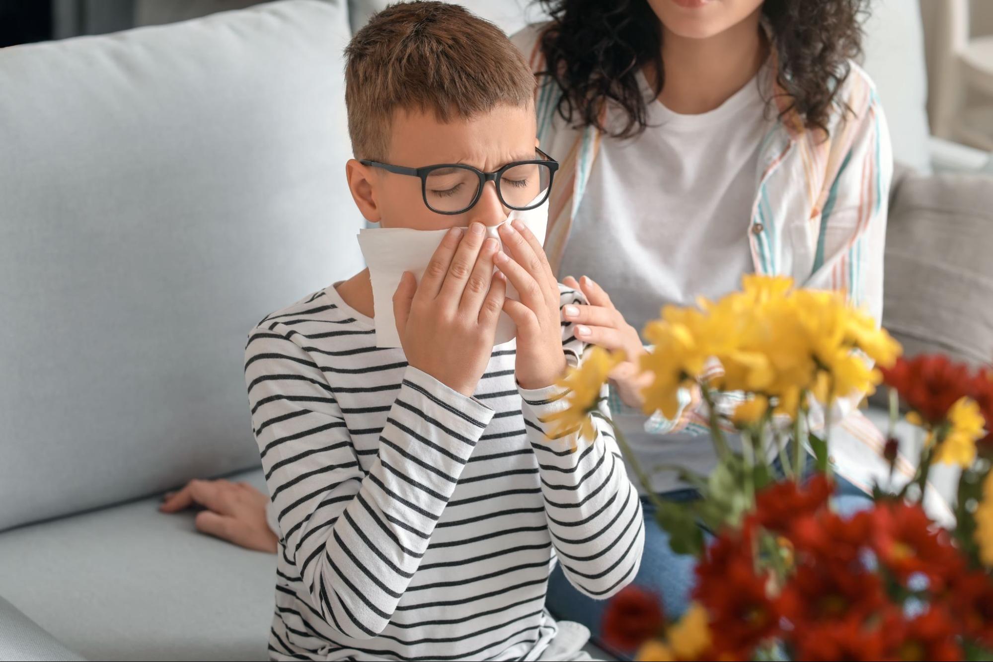 Child with hay fever using a tissue near flowers