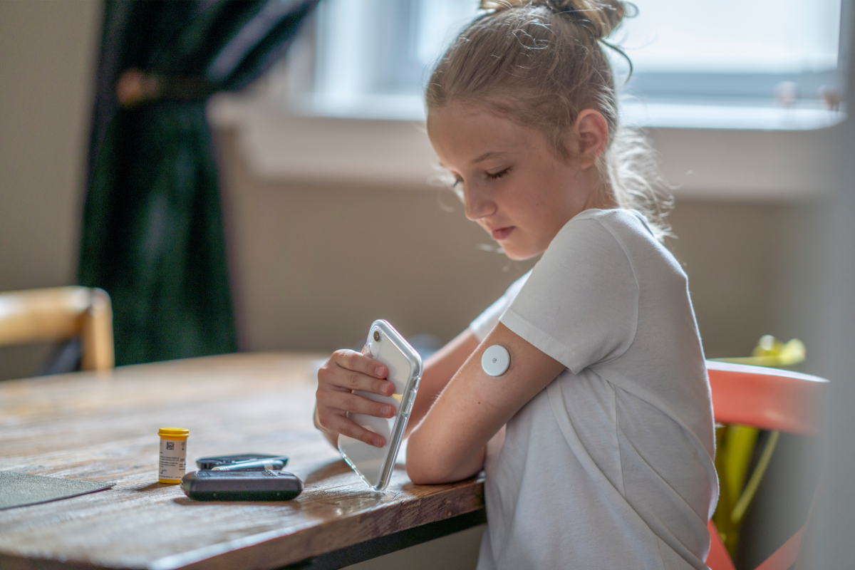 Young girl using a smartphone to scan a glucose monitor sensor on her arm.