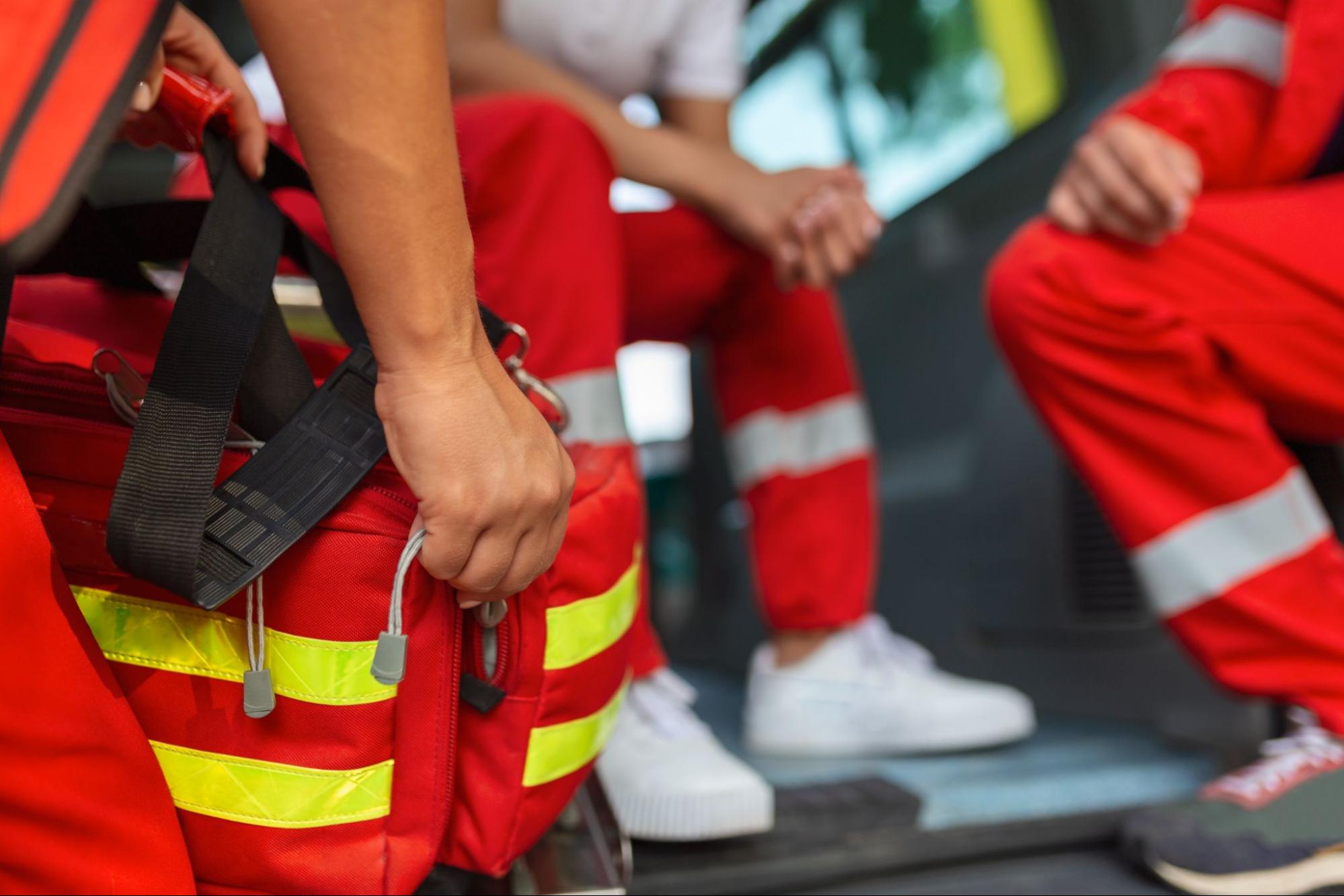 Emergency responder carrying a red first aid bag beside an ambulance